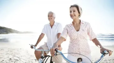 Retired couple riding bicycles together on a beach path